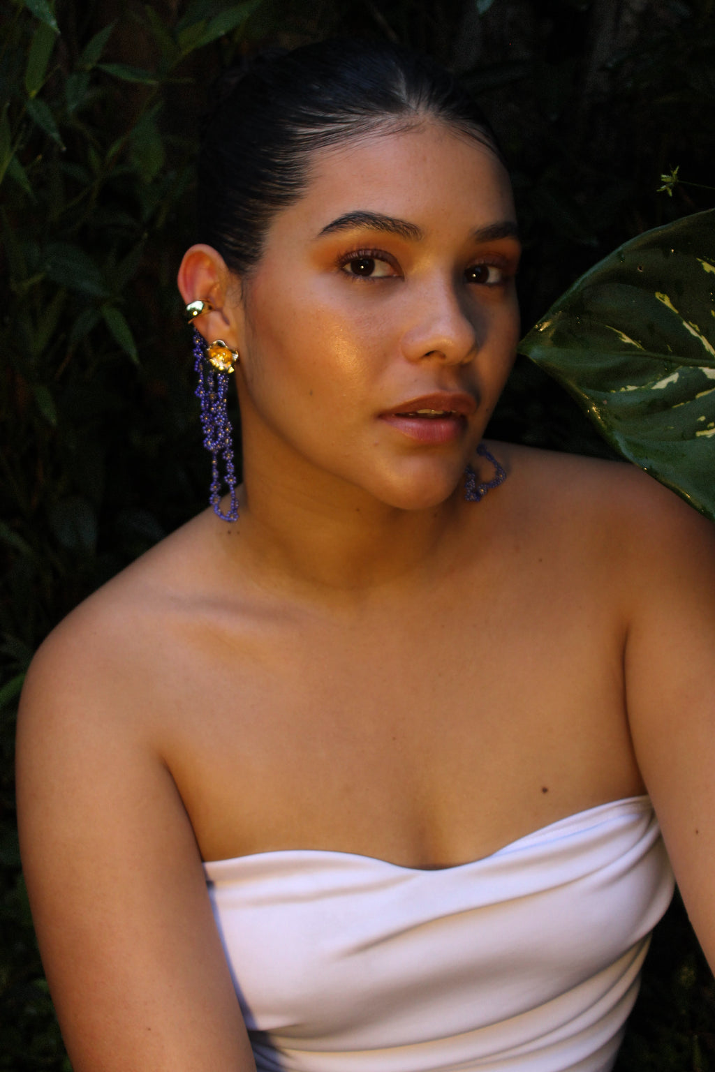 Woman wearing a strapless white dress with blue earrings against a dark background