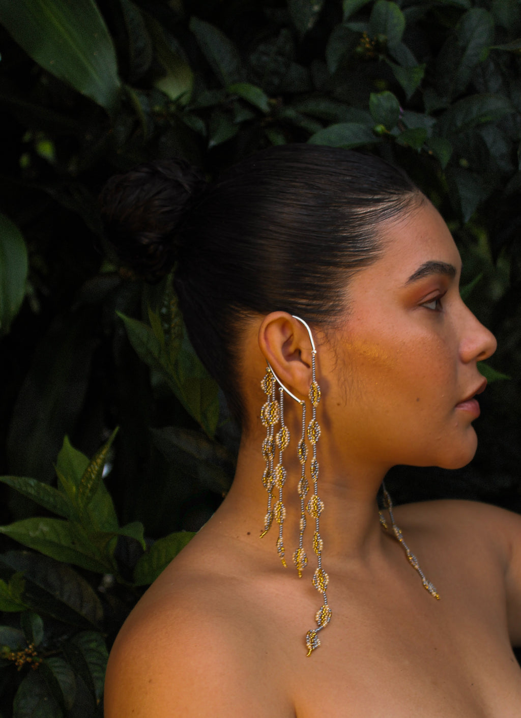 Woman wearing gold earrings with a dark green leafy background