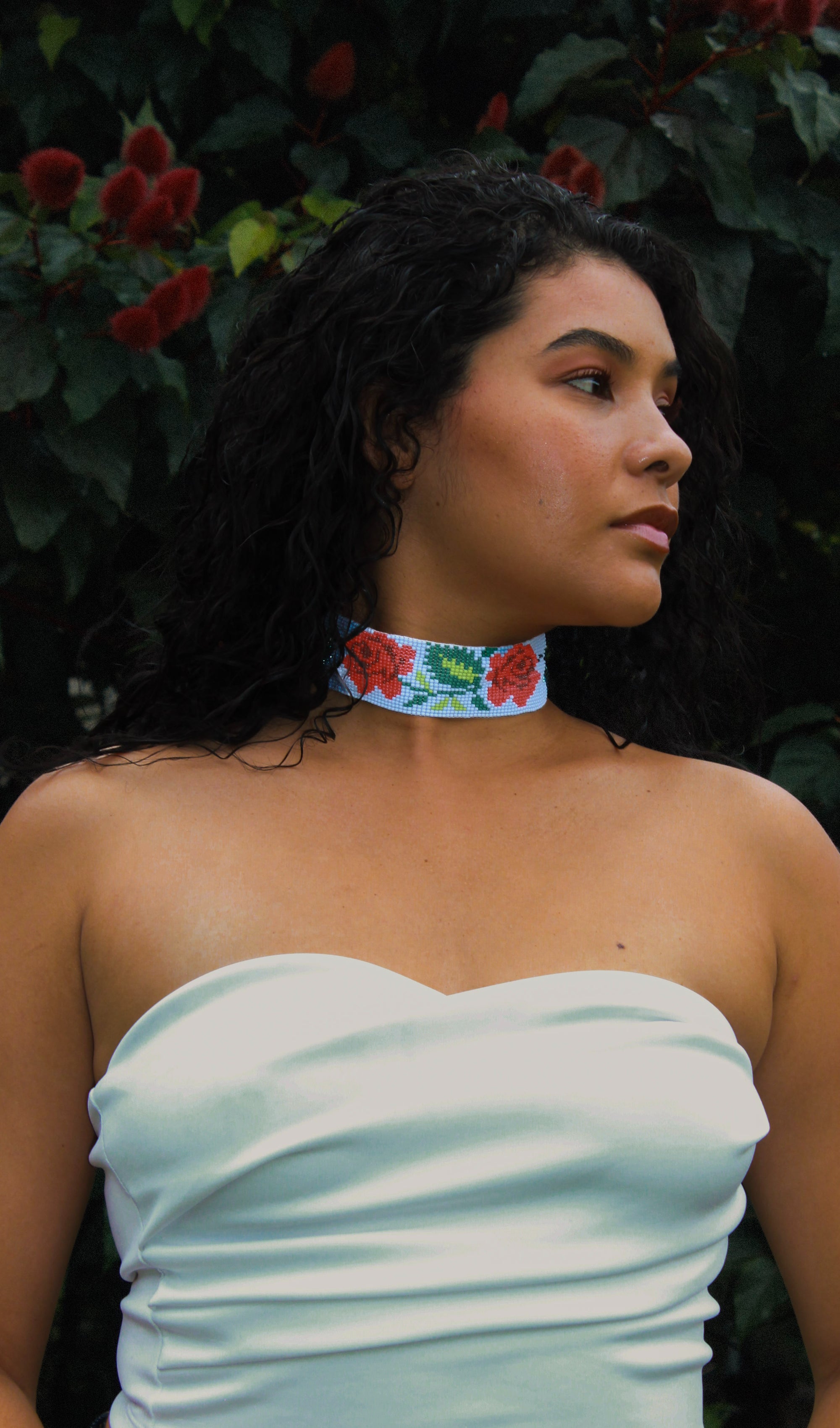 Woman wearing a strapless light blue dress with a floral choker in front of green foliage.