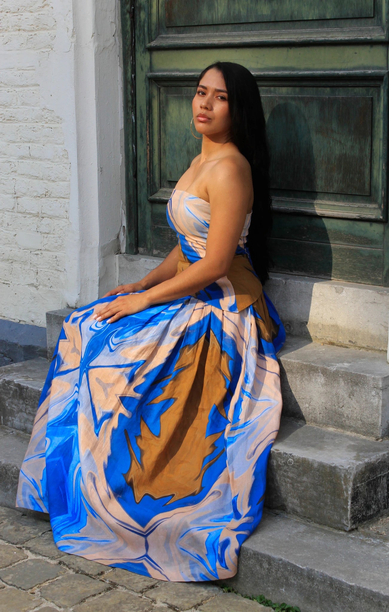 Woman in a blue and beige patterned skirt and top sitting on steps.
