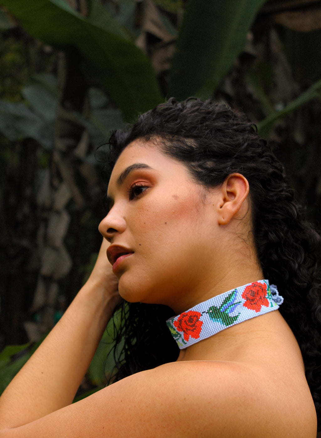 Woman wearing a colorful beaded necklace with floral design against a natural background
