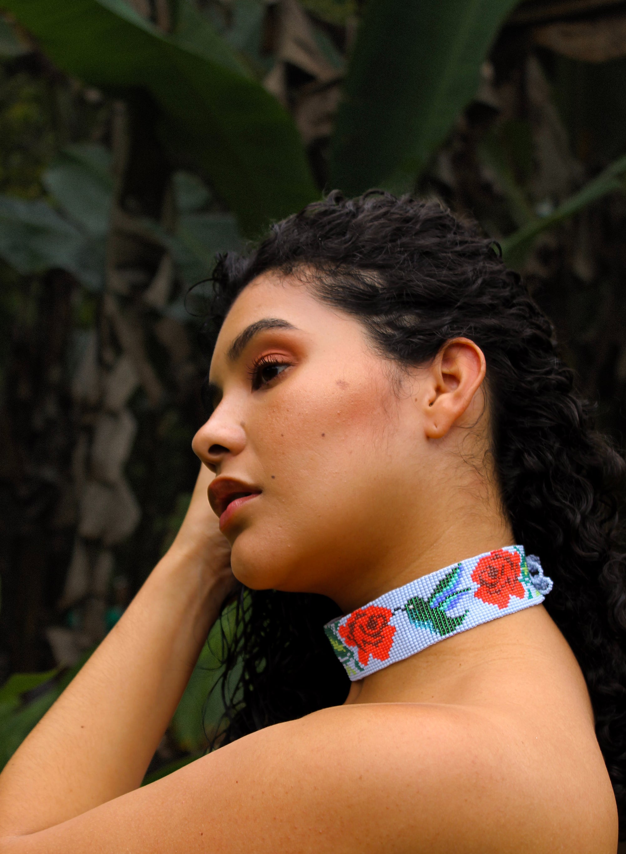 Woman wearing a colorful beaded necklace with floral design against a natural background