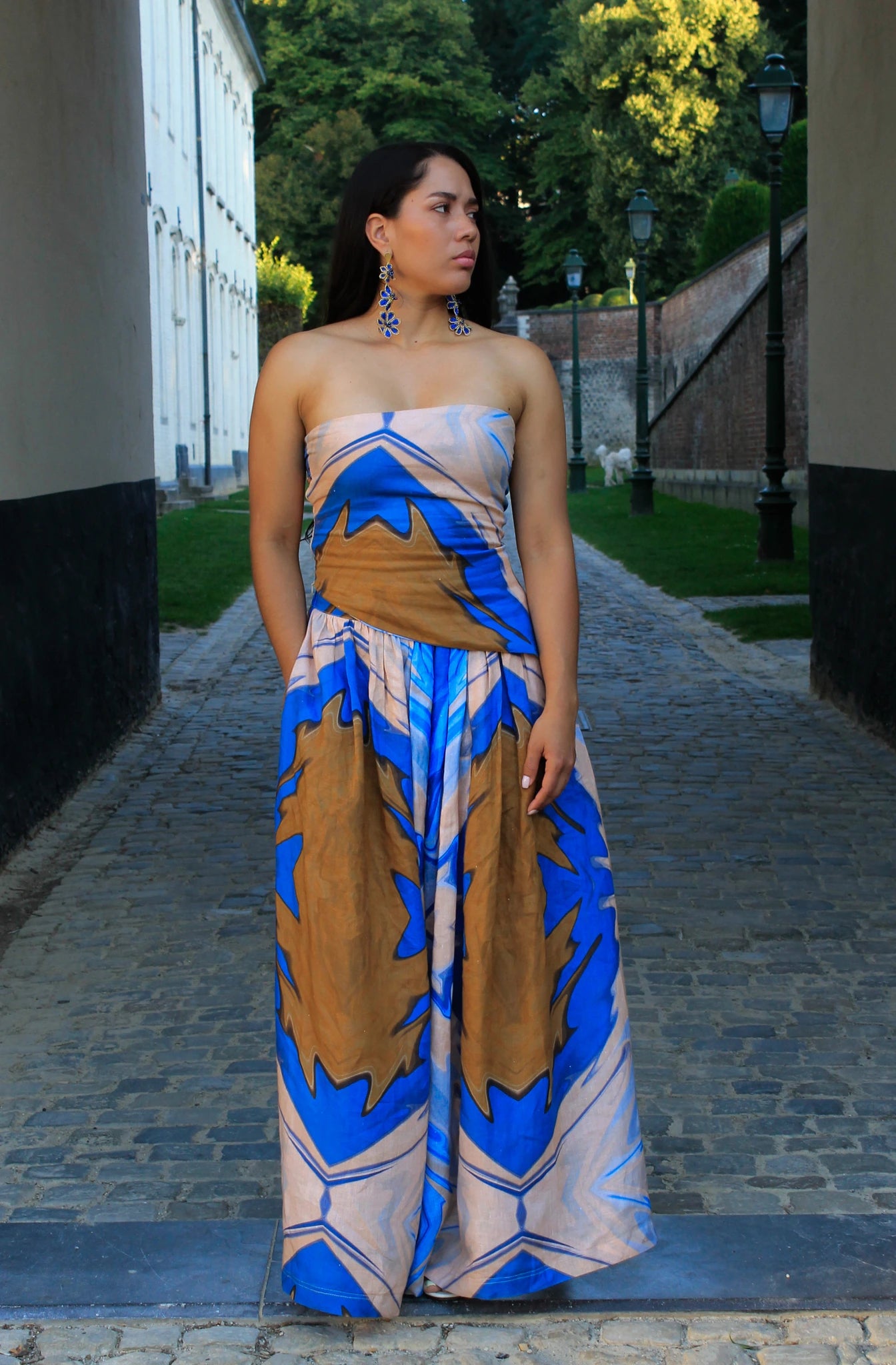 Woman wearing a strapless top with blue and brown patterns on a cobblestone street.
