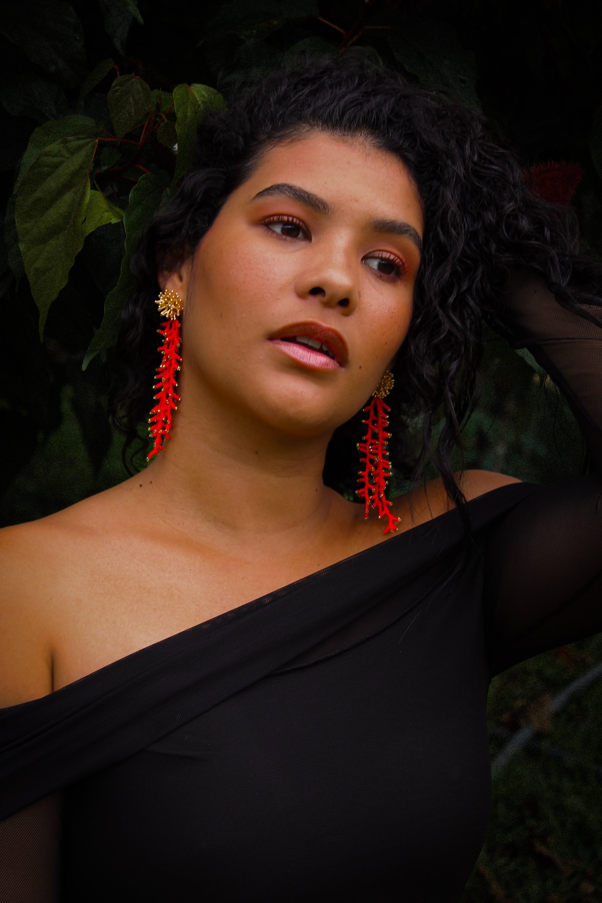 Woman wearing a black top with red earrings against a dark background