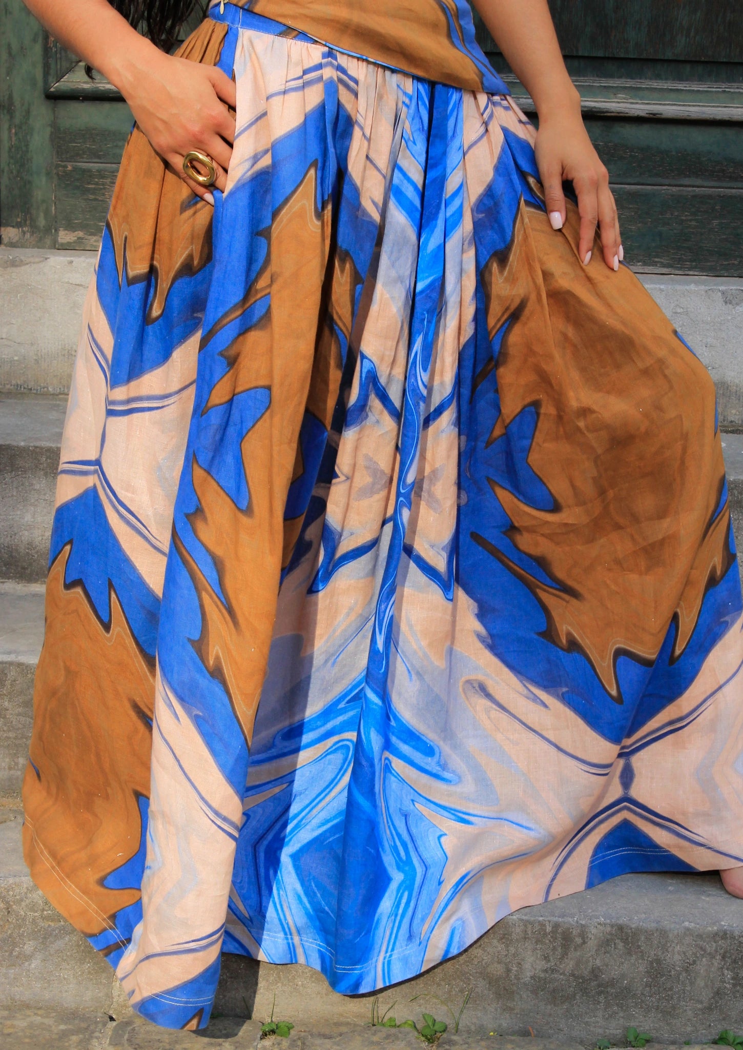 Close-up of a colorful skirt with blue and brown patterns on a person sitting on steps.