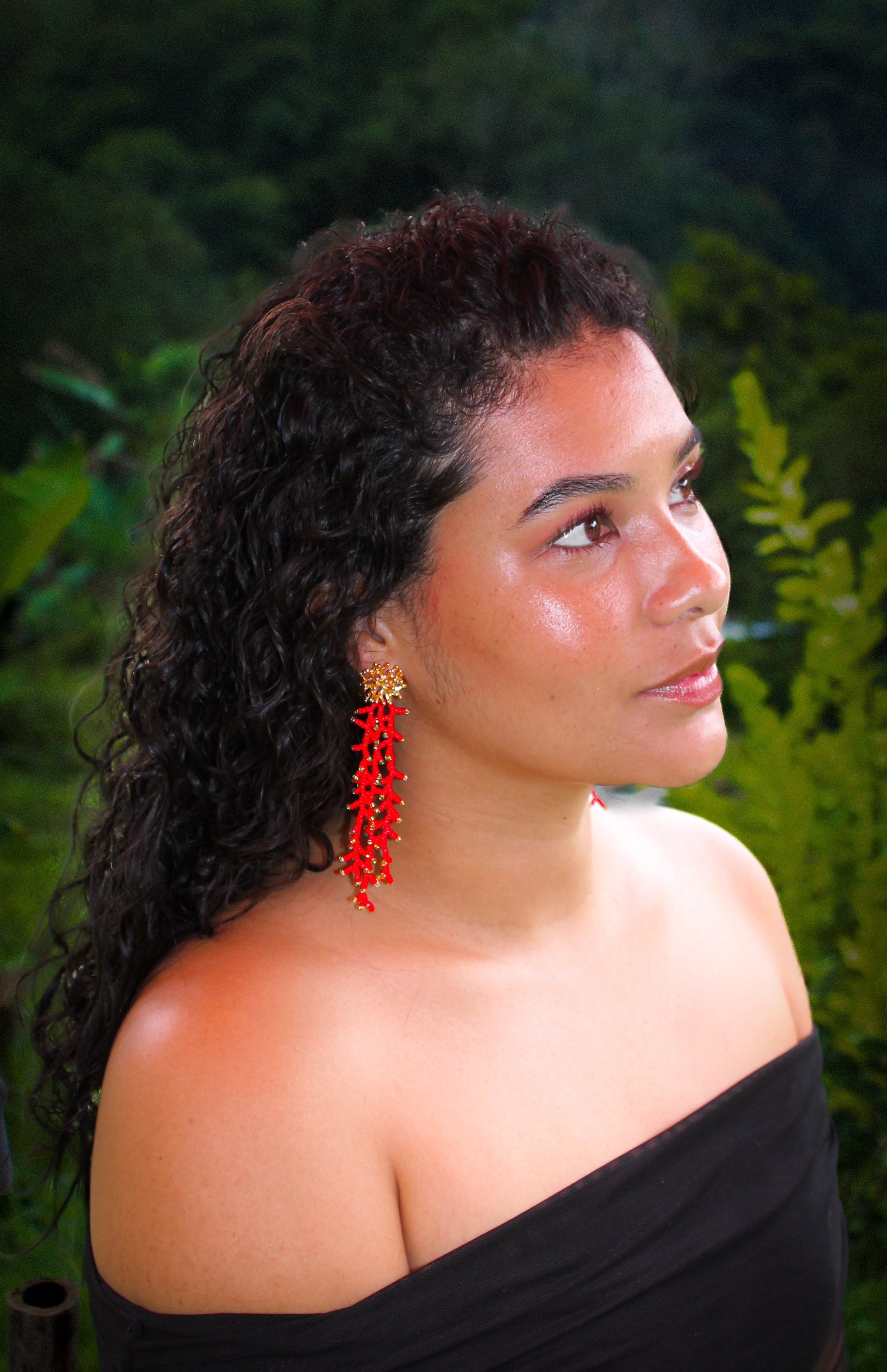 Woman with red earrings and a black top against a green outdoor background