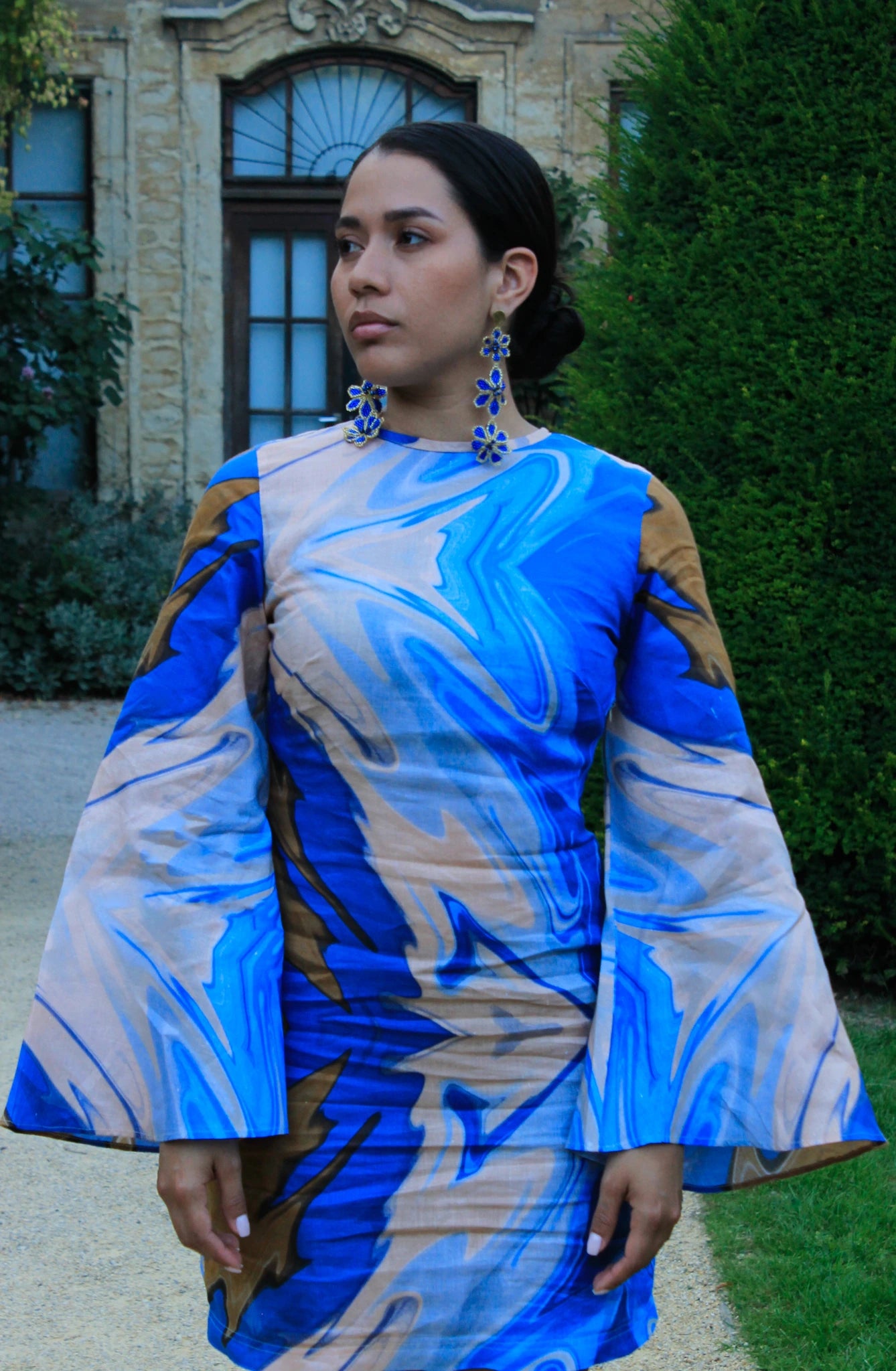 Woman wearing a blue and beige patterned dress with bell sleeves outdoors.