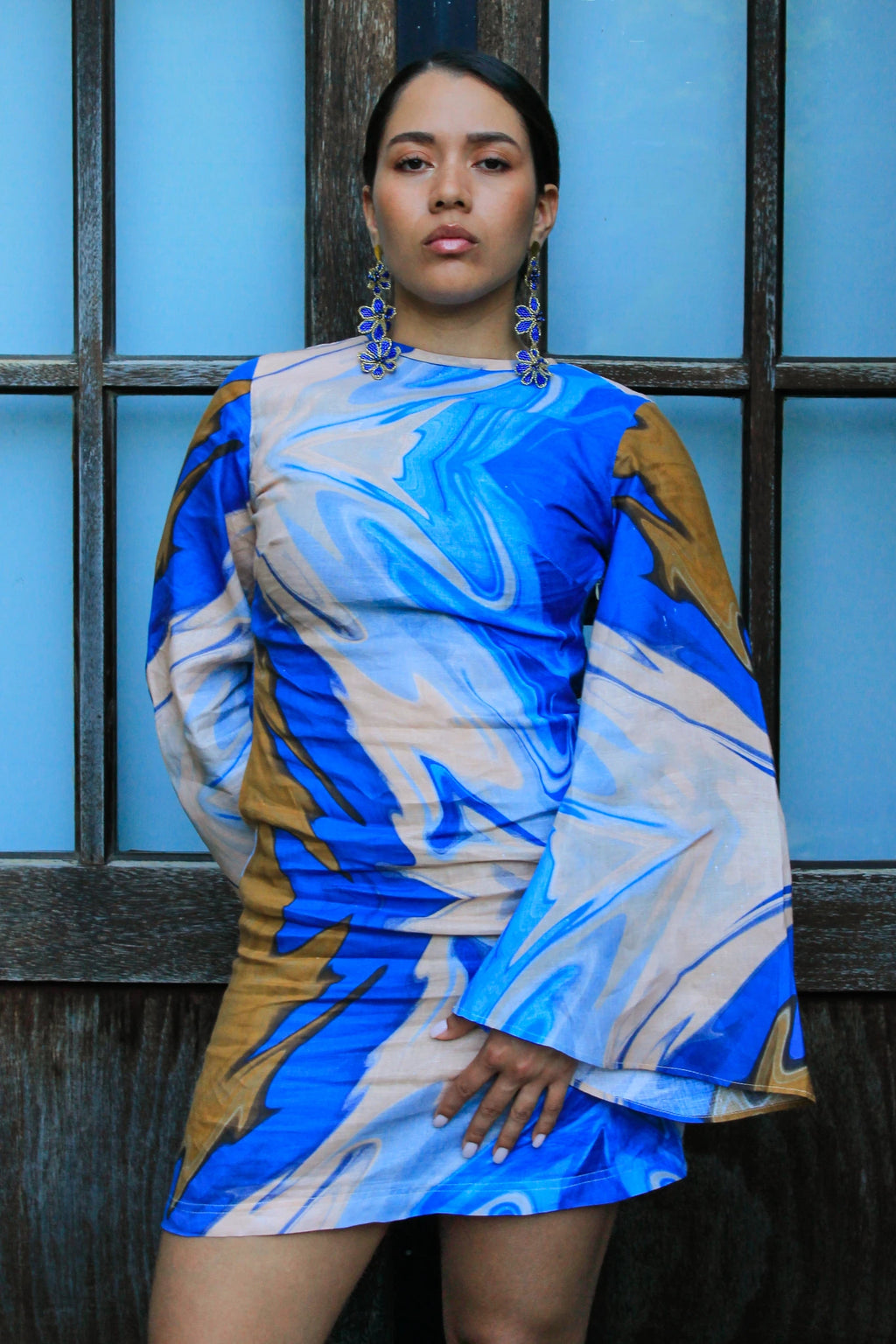 Woman wearing a blue and beige patterned dress against a blue wall.