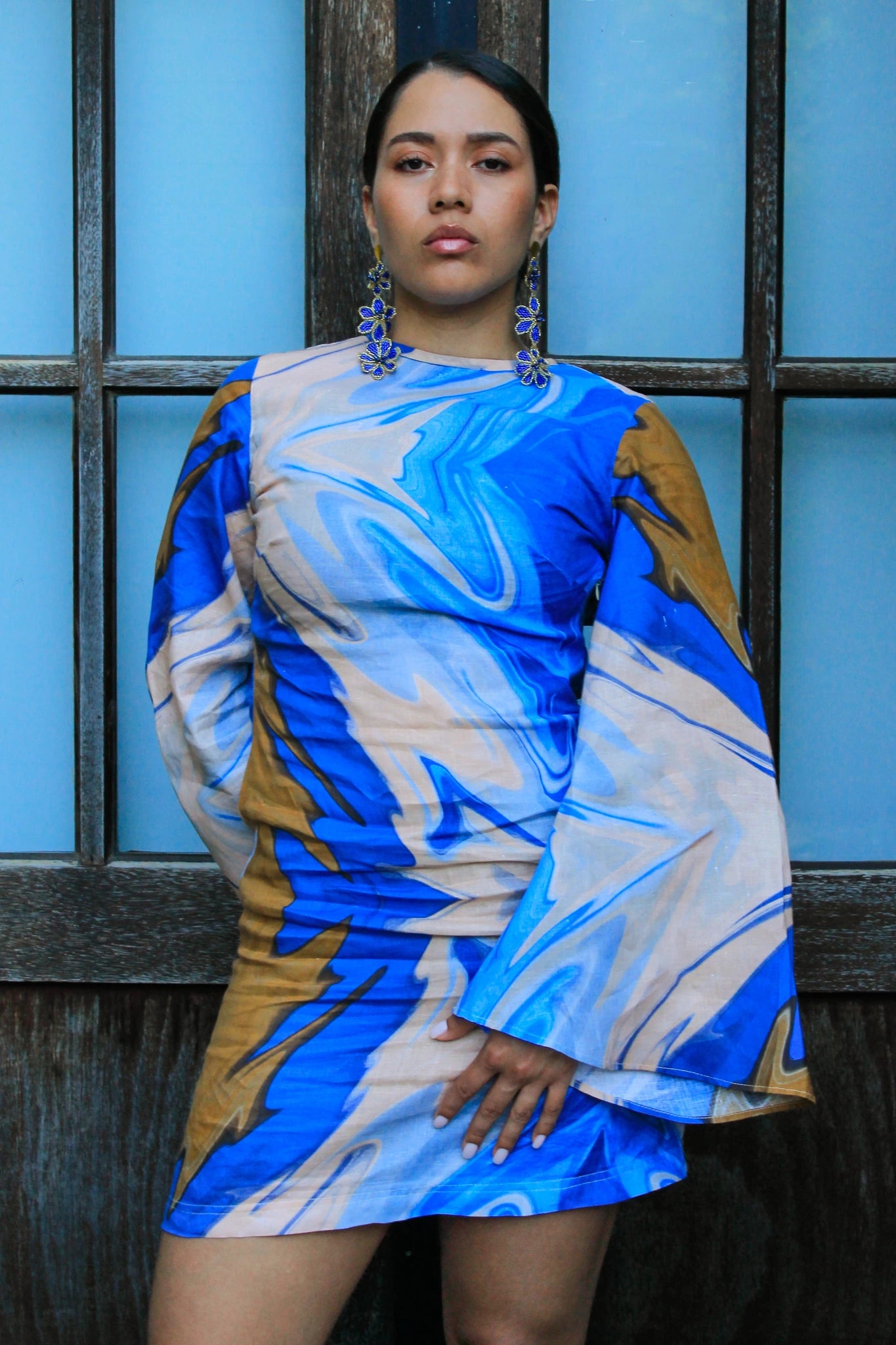 Woman wearing a blue and beige patterned dress against a blue wall.