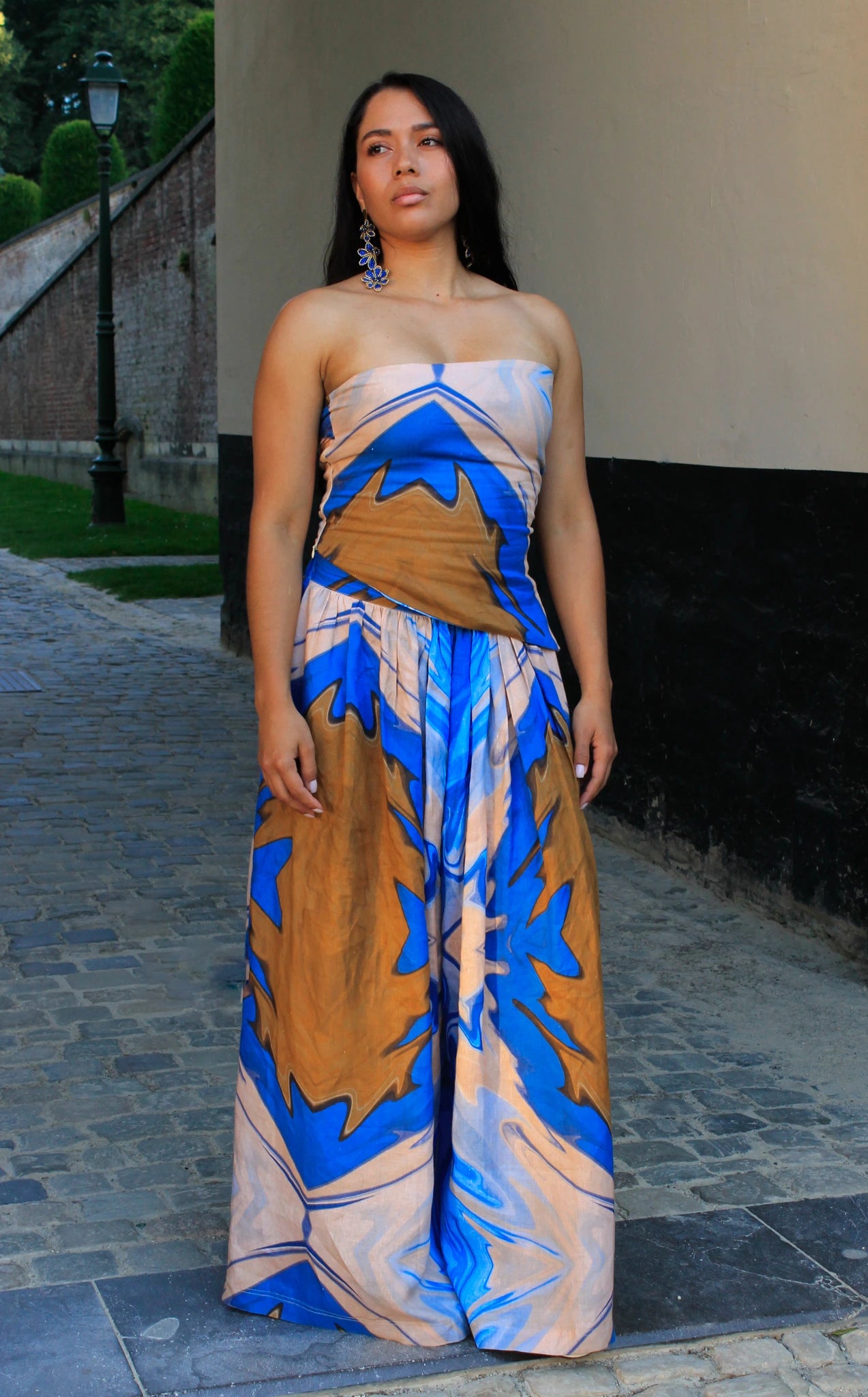 Woman wearing a strapless top with blue and brown abstract pattern on a stone path.