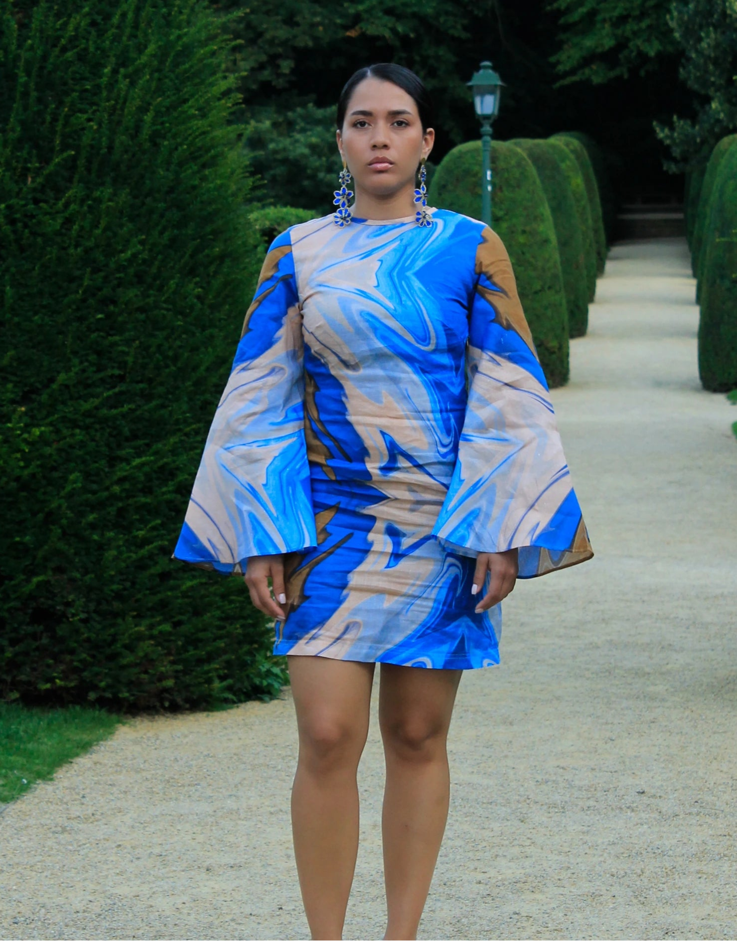 Woman wearing a blue and white patterned dress standing on a path with greenery.